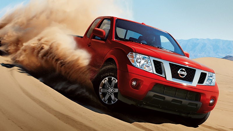Red Nissan Frontier pickup truck kicking up sand while driving on desert