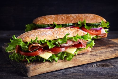 Italian sub sandwich with salami, cheese, lettuce, and tomato served on a wooden board with chips