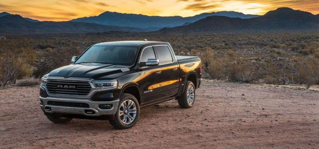 A black Ram pickup truck parked on a dirt road with mountains and a sunset in the background.