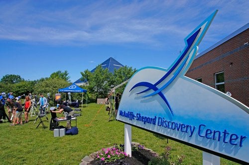 McAuliffe-Shepard Discovery Center sign with people viewing through telescopes on a sunny lawn.