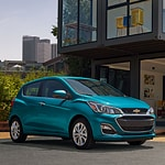 2022 Chevrolet Spark of teal color is parked infront of beautiful, glassed cover building.