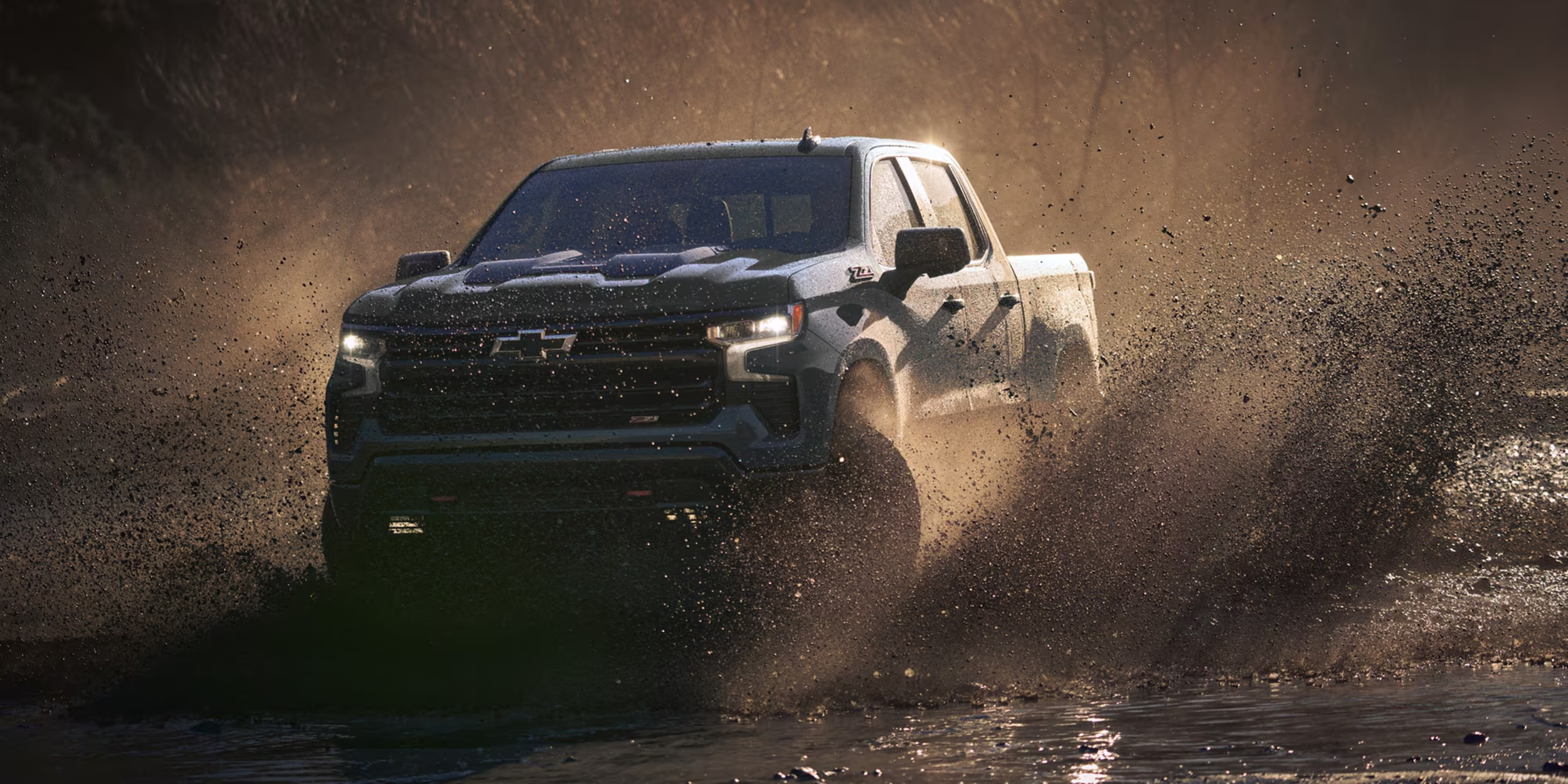 A dark gray 2024 Chevrolet Silverado HD ZR2, kicks up a rooster tail of sand in a desert landscape.