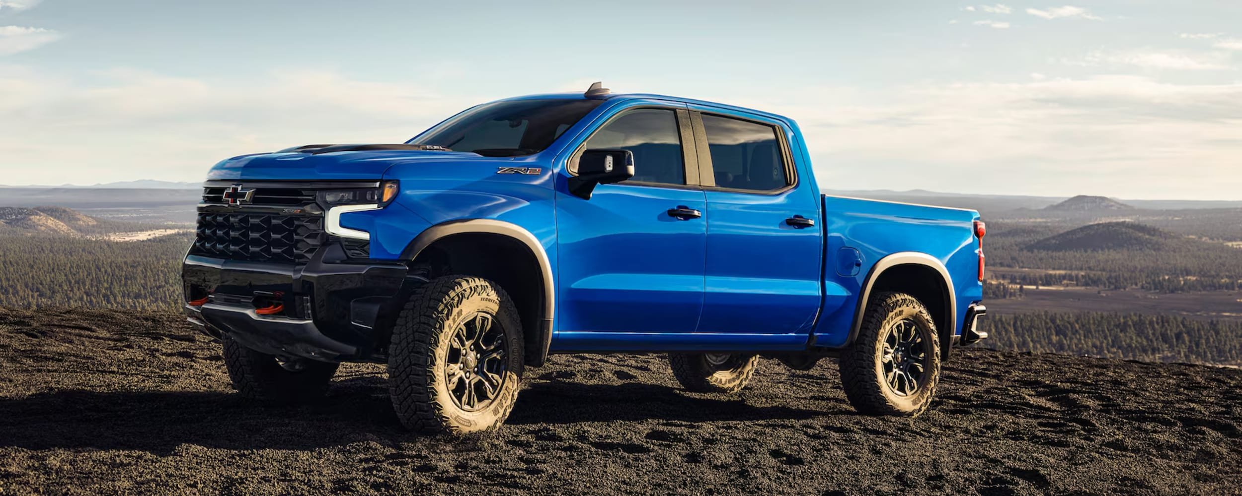 Blue Chevy Colorado driving through sand with a blur of sand.