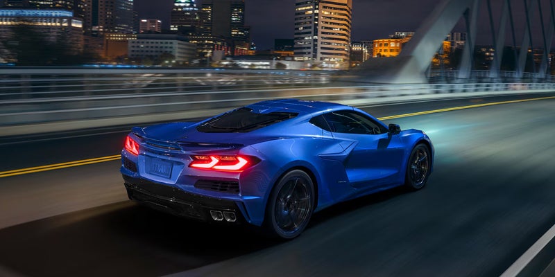 Rear view of a blue Chevrolet Corvette accelerating on a city bridge at night, tail lights glowing.