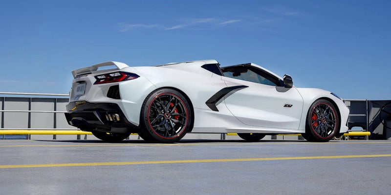 White 2023 Chevrolet Corvette Z06 convertible on a concrete parking deck with a clear blue sky.