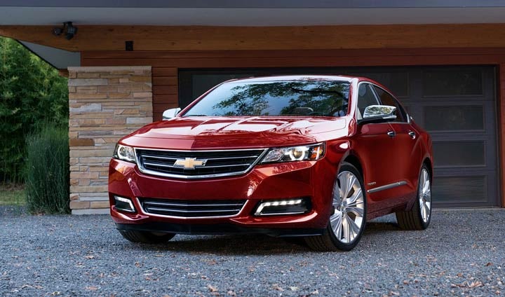 A shiny red Chevrolet Impala parked on a gravel driveway in front of a modern house.