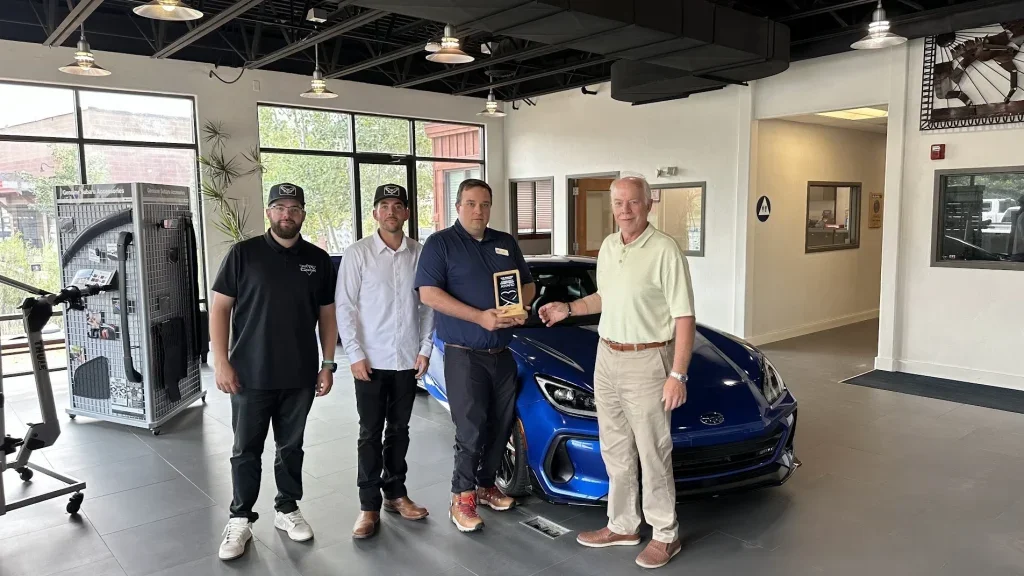 Cook Subaru team members presenting a community commitment award inside the dealership showroom.
