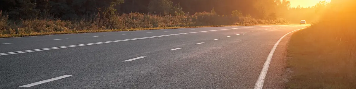 Driving on a highway through a sunny mountain landscape with lush trees.