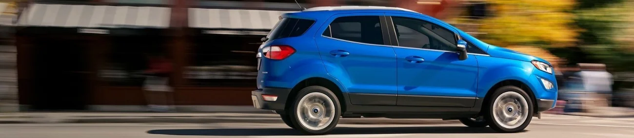 A blue SUV drives forward on a paved street near a brick building.