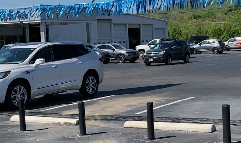 A parking lot with several SUVs; a white one in the foreground, and other cars in the background near a building with blue streamers.