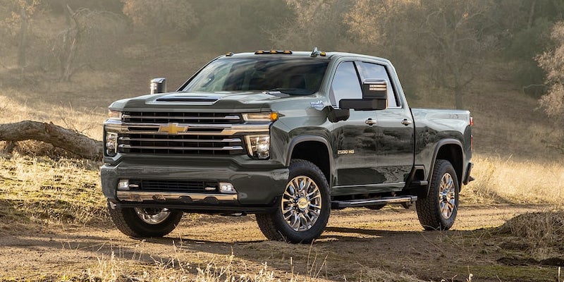 Chevy Silverado 2500 HD pickup truck on a dirt road, surrounded by dry golden grass and trees.
