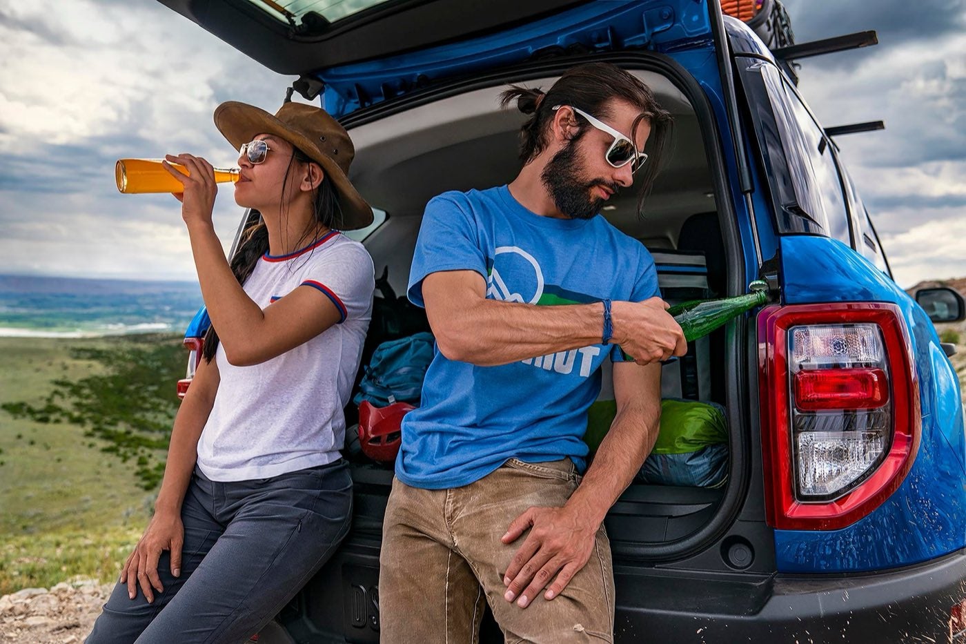 Two people leaning on the open tailgate of a Ford Bronco Sport and using its built in bottle opener, a Ford for buyers around Bowie, TX