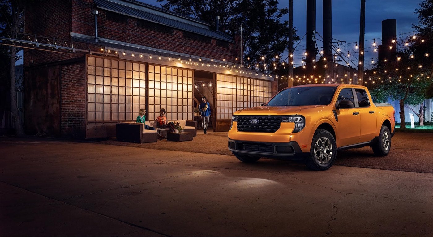 Orange Ford Maverick XLT parked under lights beside a building at night, a compact pickup option for Bowie, TX buyers