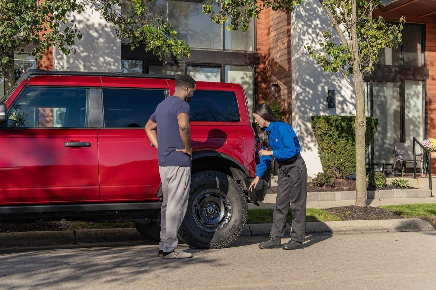 Ford service representative talking with an owner beside a red Ford Bronco parked on a street near Bowie, TX