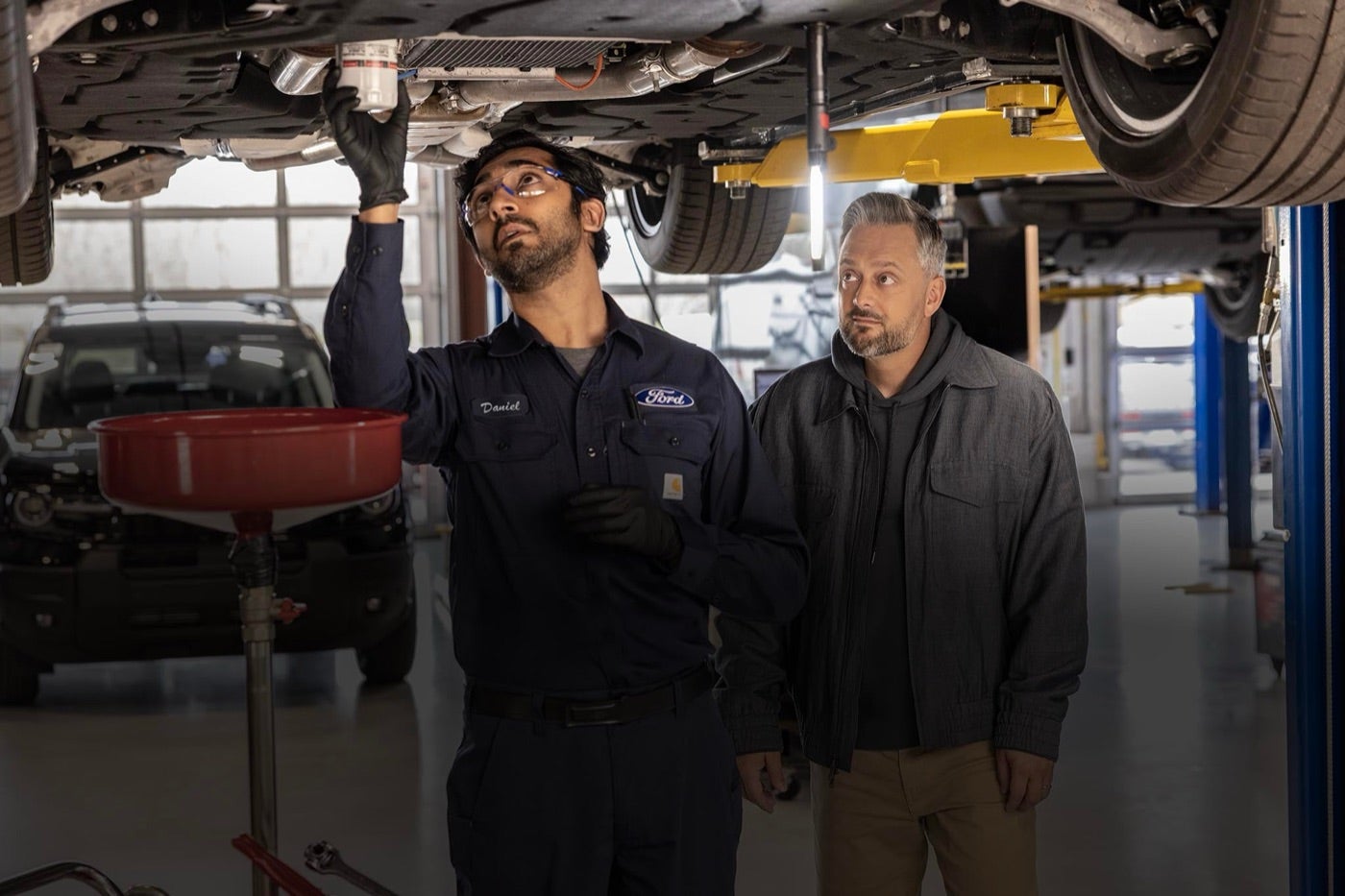 Ford technician and customer looking under a vehicle on a lift in a Bowie, TX service shop