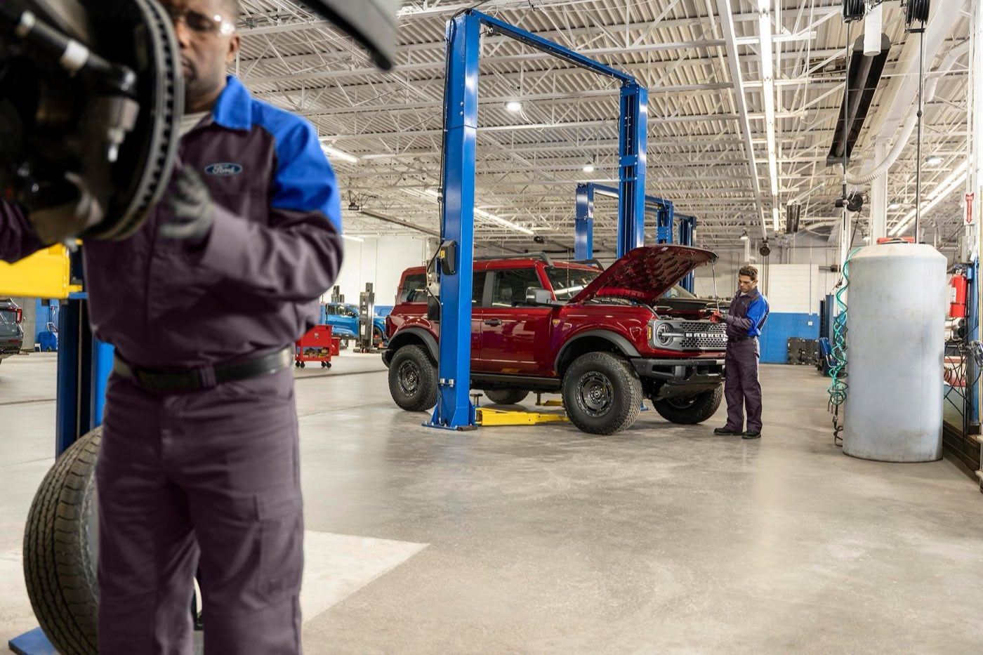 Ford technician working at a wheel in a service bay with a Ford Bronco on a lift behind him in Bowie, TX