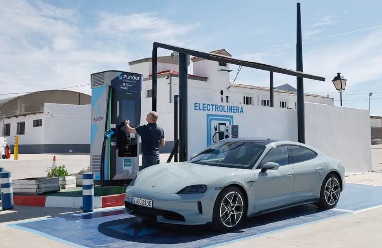 A man in a navy shirt connects a charger to a gray Porsche Taycan at a Zunder EV station.