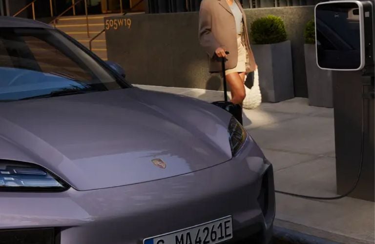 a woman with a suitcase standing next to a Porsche being charged