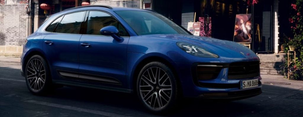 A shiny blue Porsche Macan SUV parked on a city street in front of shops.