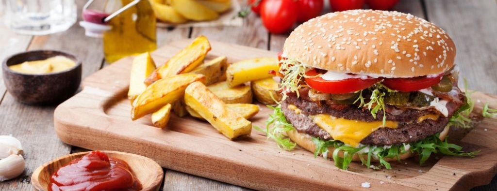 A cheeseburger with lettuce, tomato, and fries served on a wooden board