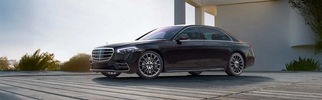 Black Mercedes-Benz S-Class sedan parked outside a modern home.