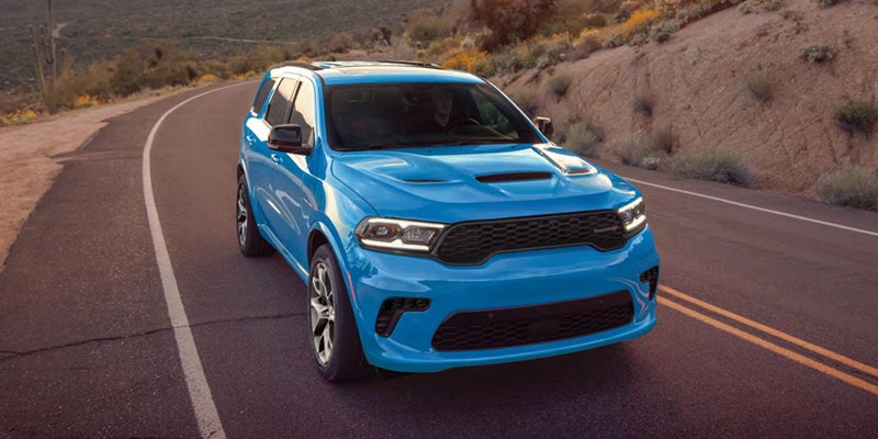 Bright blue Dodge Durango SRT Hellcat SUV driving on a winding desert road at sunset.