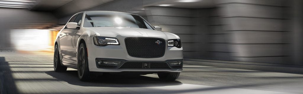 A white Chrysler 300C sedan speeds through a tunnel with motion blur in the background.