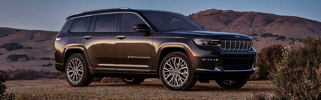 Dark gray Jeep Grand Cherokee Laredo SUV parked on a gravel road, with rolling hills in the background.