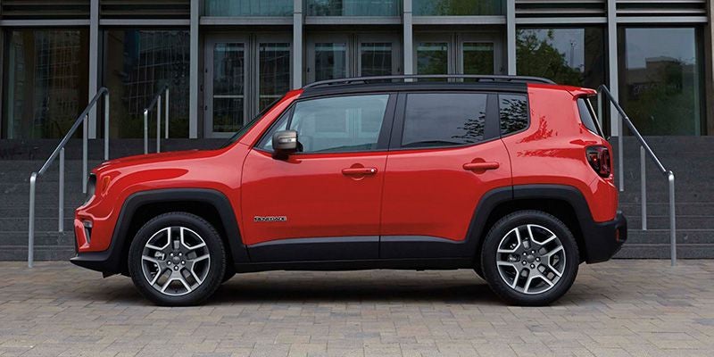 Side view of a bright orange Jeep Renegade SUV parked on a paved area in front of a modern building.