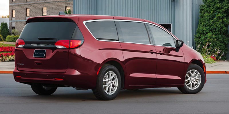 Rear three-quarter view of a dark red Chrysler Pacifica minivan parked on a grey asphalt road.