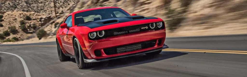 A red sporty car with a black hood speeding on a winding road with desert mountains in the background.
