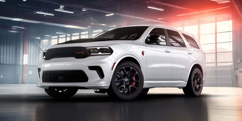 White Dodge Durango SRT Hellcat SUV parked in a garage with red lighting, viewed from the front quarter.
