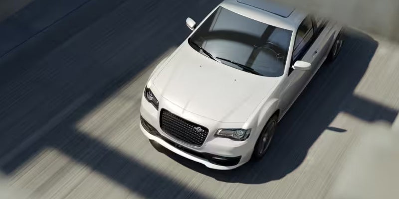 Overhead shot of a white Chrysler 300 sedan driving on a highway, casting a sharp shadow.
