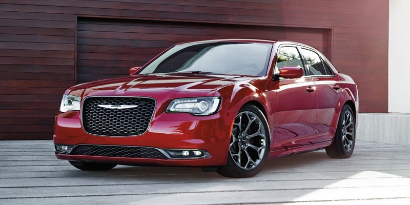 Front three-quarter view of a shiny cranberry red Chrysler 300 sedan parked in a driveway.