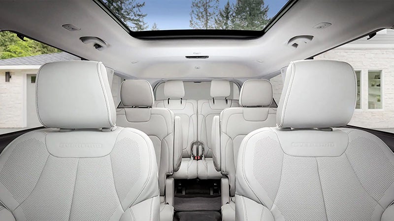 The spacious light gray interior of a seven-seater SUV, with a panoramic sunroof and three rows of seats.