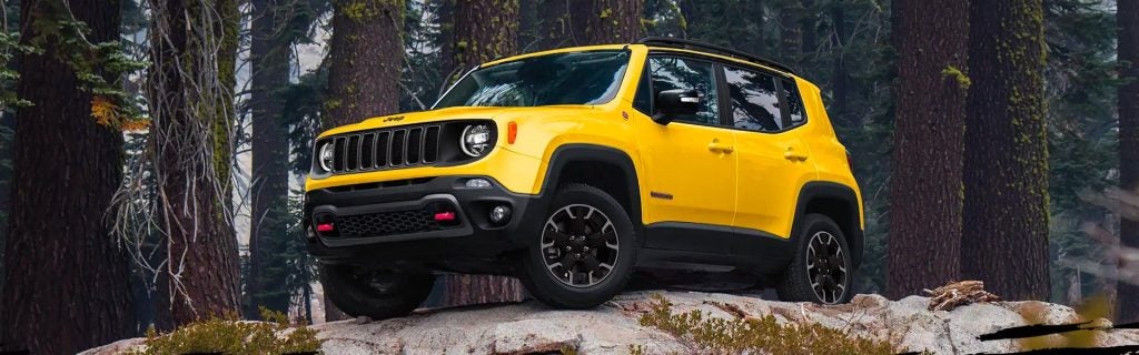 A bright yellow Jeep Renegade with a black roof rack on a rocky, wooded hill.