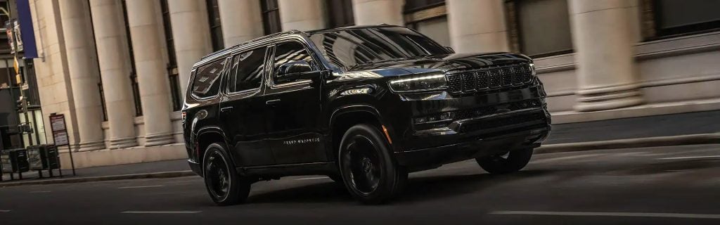 A black SUV drives on a city street past a building with large stone columns.