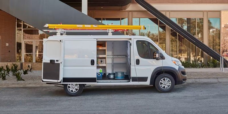 A white commercial cargo van with the back doors and side sliding door open, revealing shelving inside.
