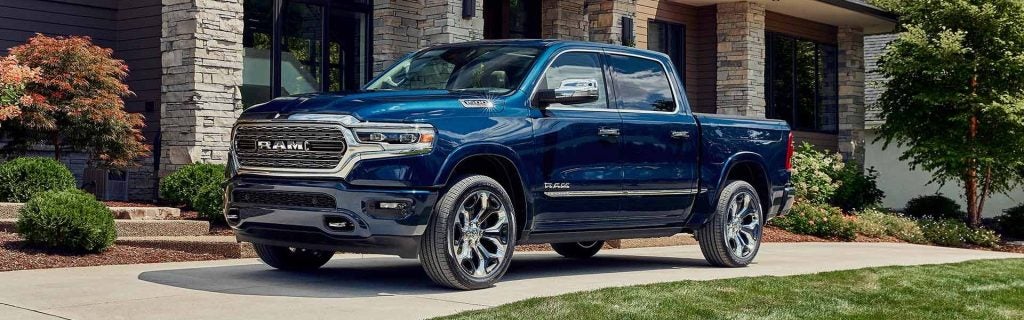 A shiny, dark blue Ram 1500 truck with chrome wheels is parked on a driveway in front of a modern house.