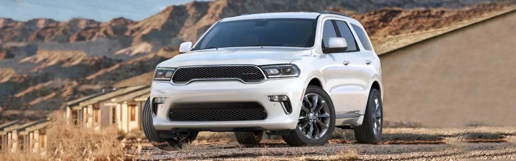 White Dodge Durango parked on a dirt road with mountains and desert homes in the background.