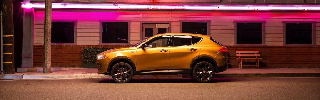 A golden orange crossover SUV parked at night with pink neon lights from the building reflecting on its side.