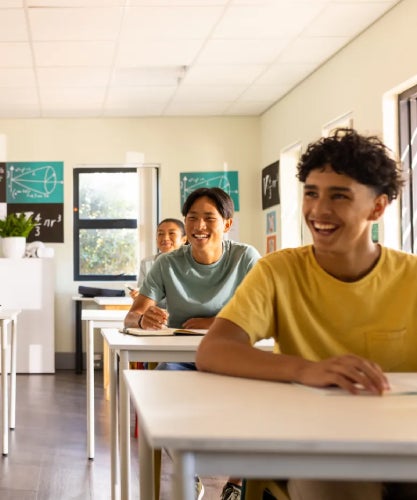 Students smiling and sitting at desks in a bright classroom