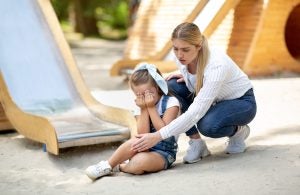 Mother Examining Daughter's Injured Knee After Slide Ride On Playground