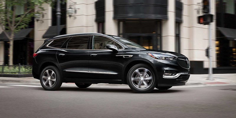 This image shows a black mid-size luxury SUV, likely a Buick Enclave, captured in motion on a city street