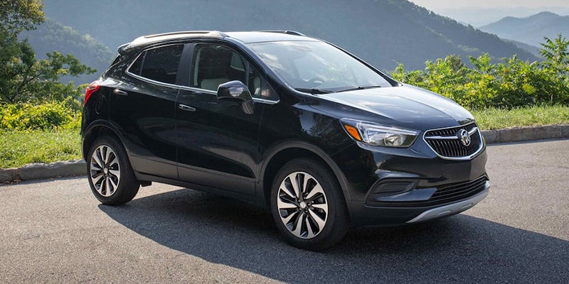 The image shows a black compact SUV/crossover vehicle parked on a paved roadside with a scenic mountainous landscape in the background