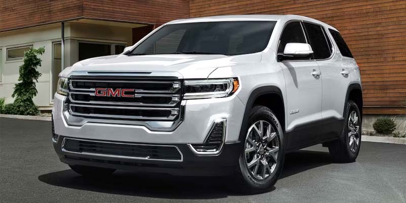 White GMC Acadia SUV parked in front of a modern house with wood siding.