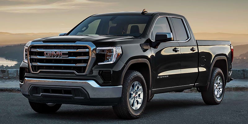 Black GMC Sierra pickup truck parked on a road with a scenic mountainous landscape in the background.
