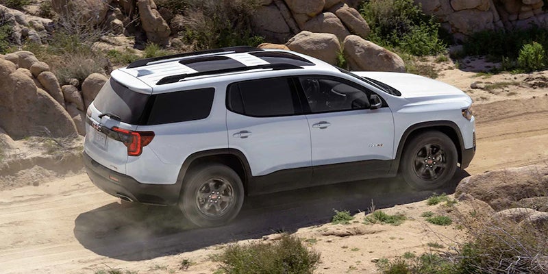White GMC SUV driving on a dusty off-road trail surrounded by rocks and desert terrain.
