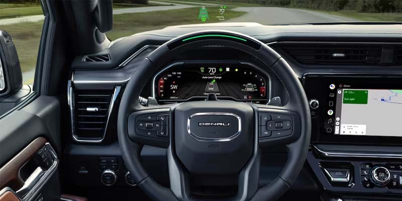 Driver’s view of a GMC Denali interior showing a steering wheel, digital instrument cluster with navigation and speed display