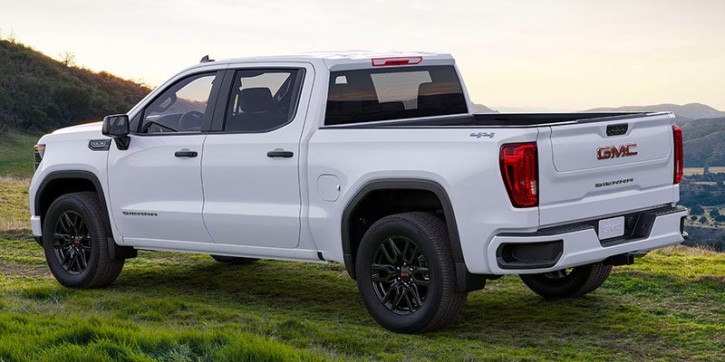 White GMC Sierra pickup truck with black wheels parked on a grassy hill